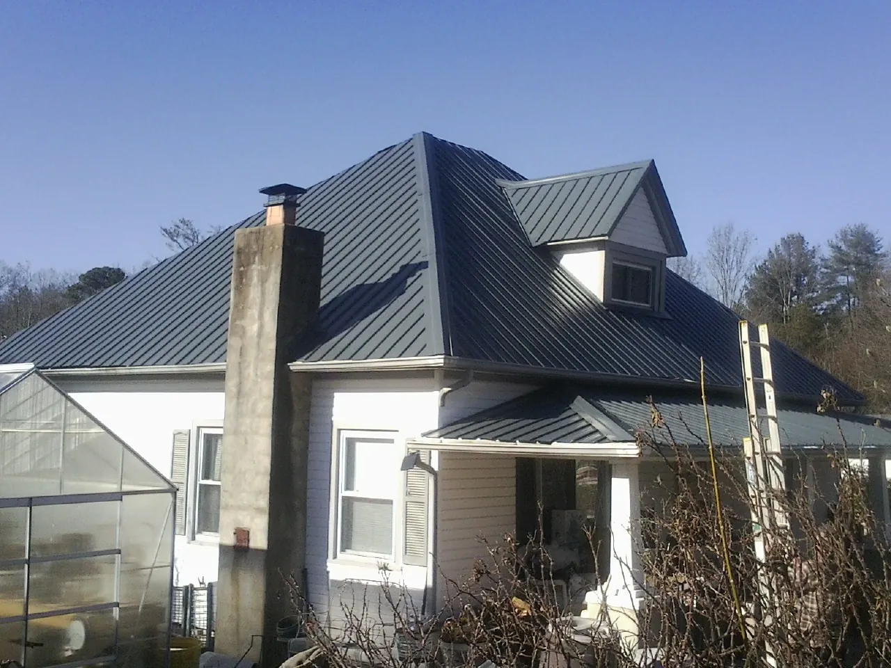 Dark blue standing seam metal roof on a white farmhouse with dormer — Slate & Tile Roof Repair by Roofing Brothers in Doty