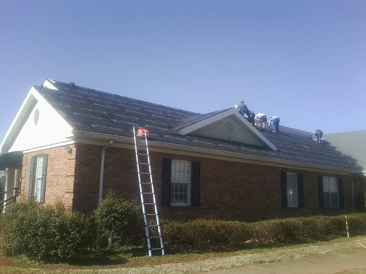 Crew tearing shingles off a brick ranch roof with a ladder set — Emergency Roof Repair work by our crew in Doty