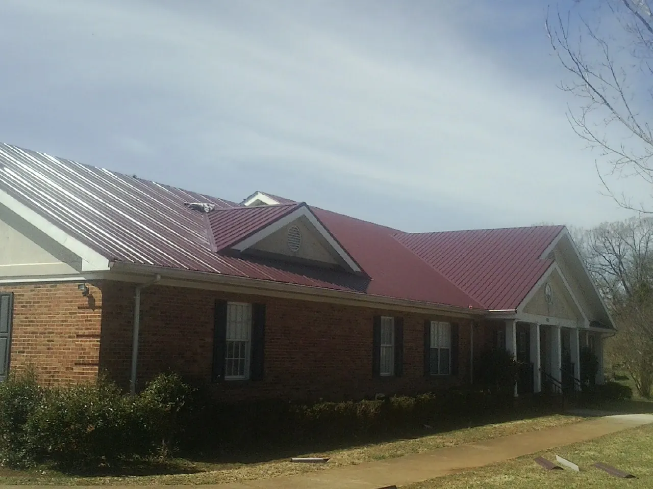 Red metal roof with gabled entries on a long brick building, from a Hail Damage Roof Repair job in Doty