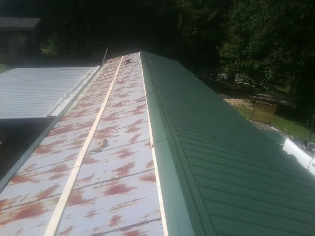 Old rusted panels beside newly installed green metal roofing — Wind Damage Roof Repair by Roofing Brothers in Doty