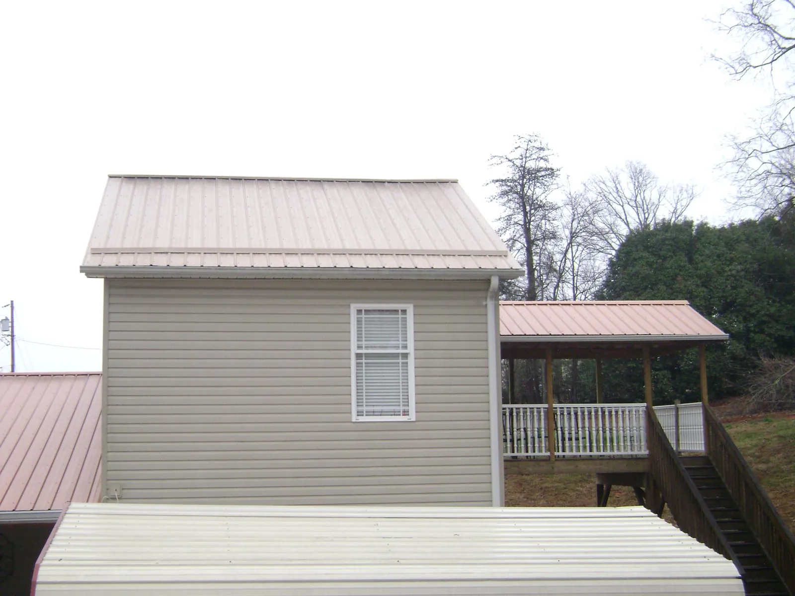 Tan metal roofs on a two story addition and attached porch, from a Roof Replacement job in Doty